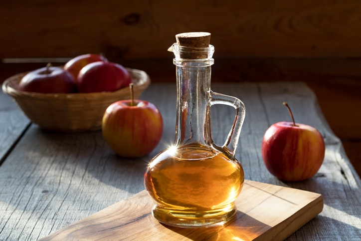 A bottle of apple cider vinegar in the morning sun, with apples in the background