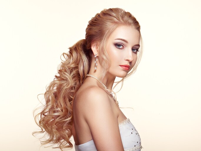 Blonde Girl with Long and shiny Curly Hair. Beautiful Model Woman with Curly Hairstyle. Care and Beauty Hair products. Perfect Make-Up and Jewelry