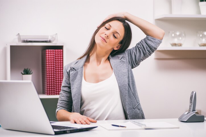 Young businesswoman is relaxing in her office. She is stretching her body.