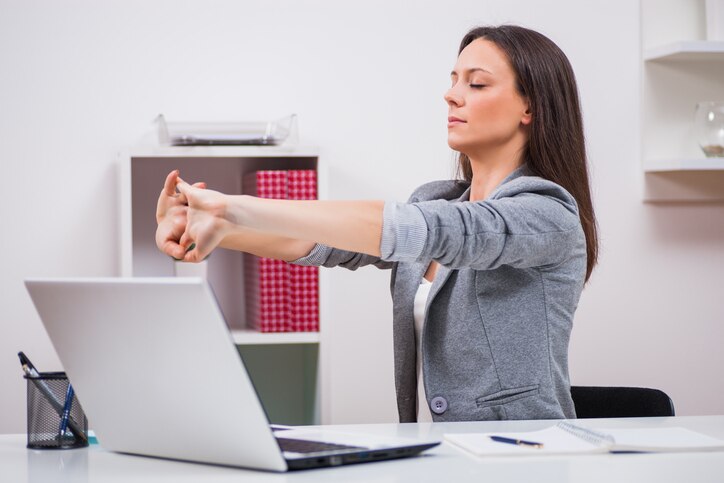 Young businesswoman is relaxing in her office. She is stretching her body.