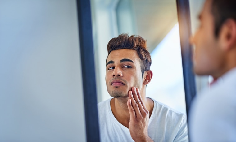 Shot of a handsome young man admiring looking at his face in the bathroom mirror