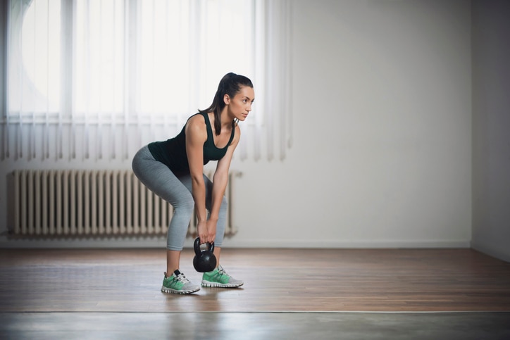 Beautiful young woman doing kettlebell deadlifts at home.