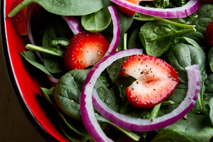 Delicious fresh spinach salad with red onion, ripe strawberries and cracked black pepper.