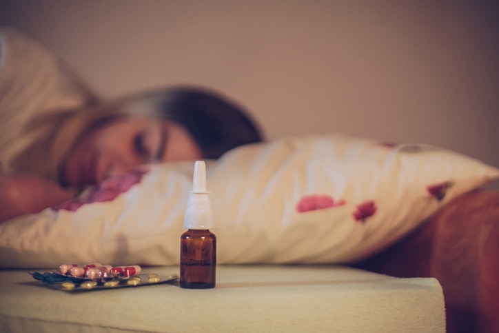 Sick woman lying in bed with pills in front