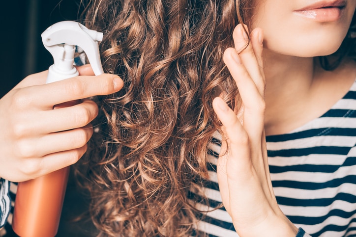 Woman applying spray on curly brown hair close-up