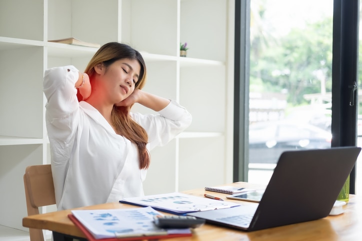 Asian businesswoman touching massaging stiff neck to relieve pain in muscles working in incorrect posture.