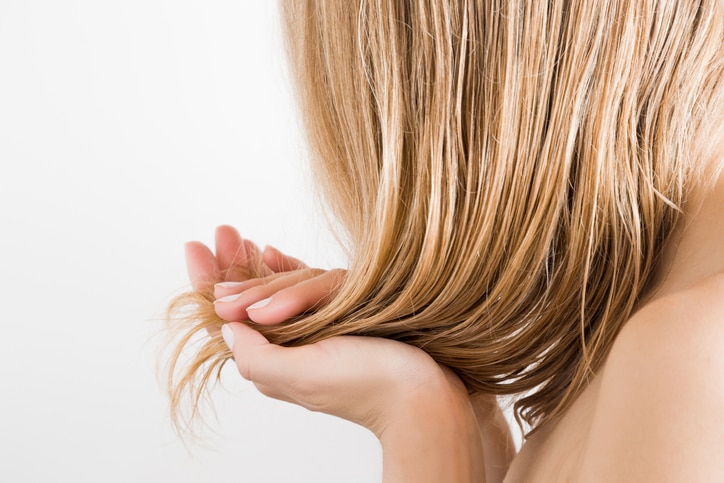 Young woman with hand touching her wet, blonde, perfect hair after shower on the white background. Care about beautiful, healthy and clean hair. Beauty salon concept. Side view.