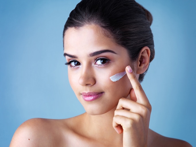 Studio portrait of a beautiful young woman applying face cream against a blue background