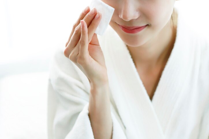 Woman applying cleansing lotion to face, using cotton wool pad