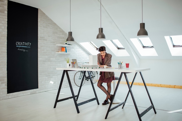 Female architect working in her new modern office. Standing and examining blueprints for her new project.