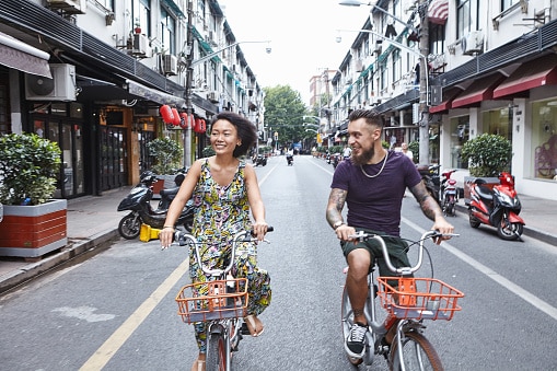 Multi ethnic hipster couple cycling along city street, Shanghai French Concession, Shanghai, China