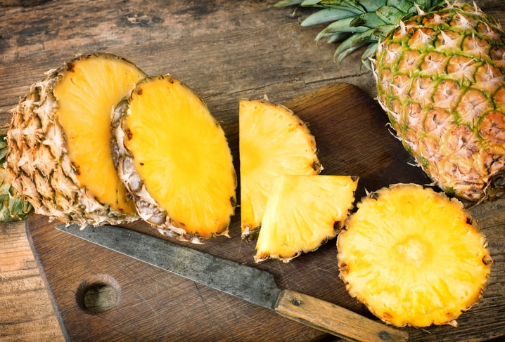 one whole and one sliced pineapples on wooden background