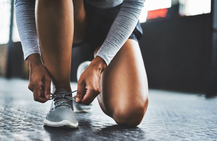 Cropped shot of a woman tying her shoelaces in a gym