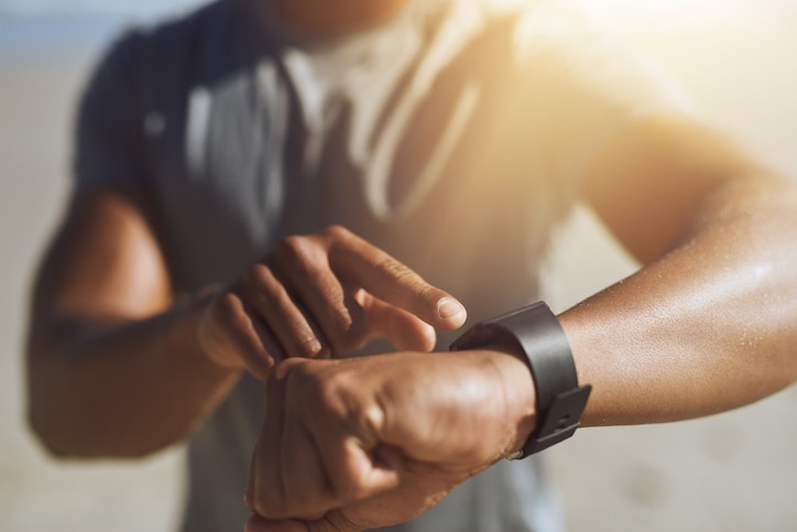 Portrait of a competitive, athletic young man ctracking his performance with an app on smart watch while running off road outdoors through the woods on a trail in the afternoon wearing sportswear.