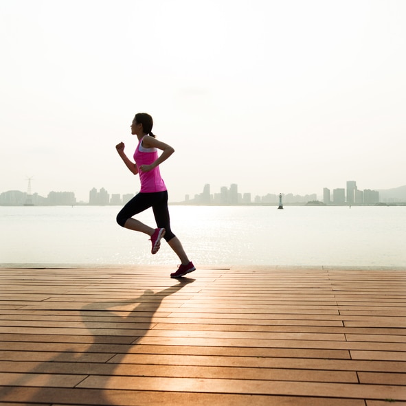 Young woman running at wooden boardwalk, sunset.