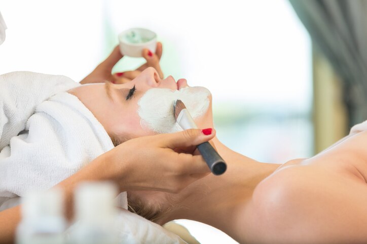 Esthetician applying face mask to spa client during facial