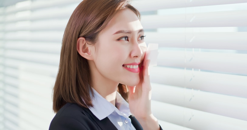 Young asian businesswoman smile and use oil blotting paper on her face