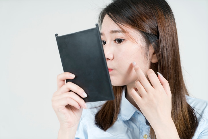 young business woman looking concerned at herself in hand mirror.