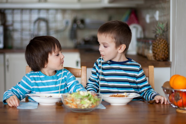 Two sweet children, boy brothers, having for lunch spaghetti at home, enjoying tasty food