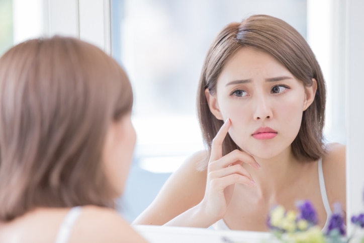 woman look mirrior feel upset and touch her face with acne problem