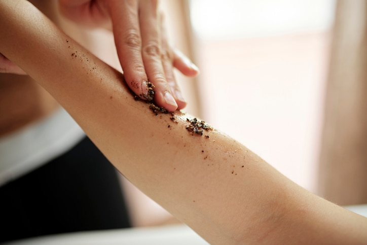 Masseur applying apricot kernel scrub to exfoliate skin of of young woman