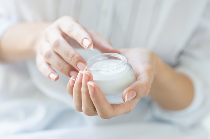 Closeup shot of hands applying moisturizer. Beauty woman holding a glass jar of skin cream. Shallow depth of field with focus on moisturizer.