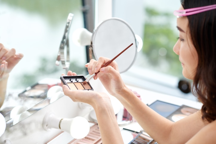 Young woman applying make-up in front of mirror in the morning