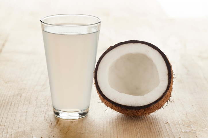 "A high angle close up of half a coconut and a tumbler full of coconut water, coconut water is said to be rich in potassium and antioxidants. Shot on a grungy old wooden table."