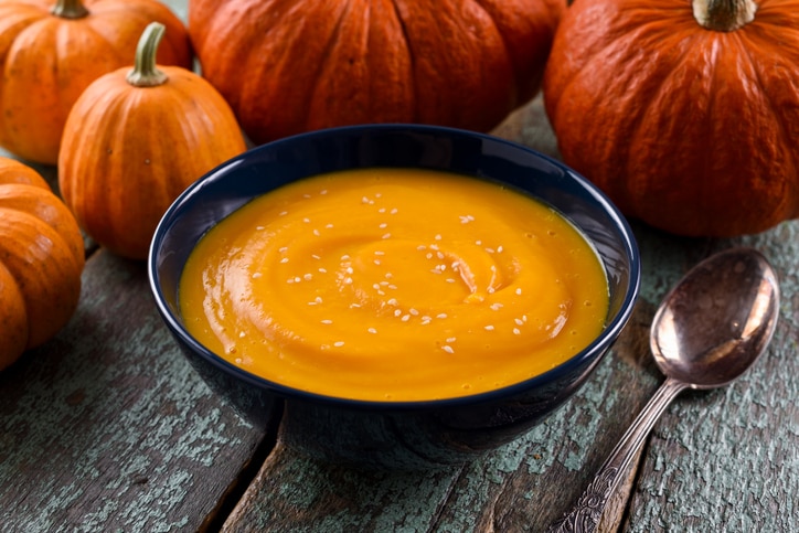 Healthy vegetarian meal. Simple pumpkin soup with sesame seeds decorated with bright orange pumpkins on shabby blue background closeup