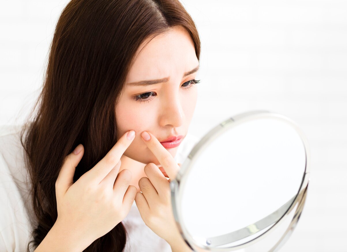 young woman squeeze her acne in front of the mirror