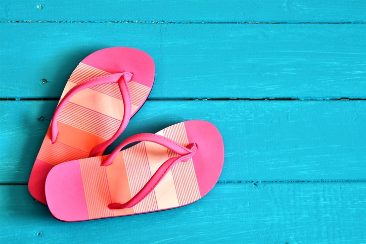 A top view image of a pair of ladies pink flip-flop sandals on a bright blue background.