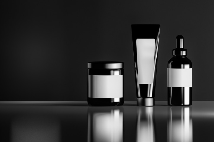 Set of black cosmetic bottles with white blank labels on the reflective shiny background. 3D illustration.