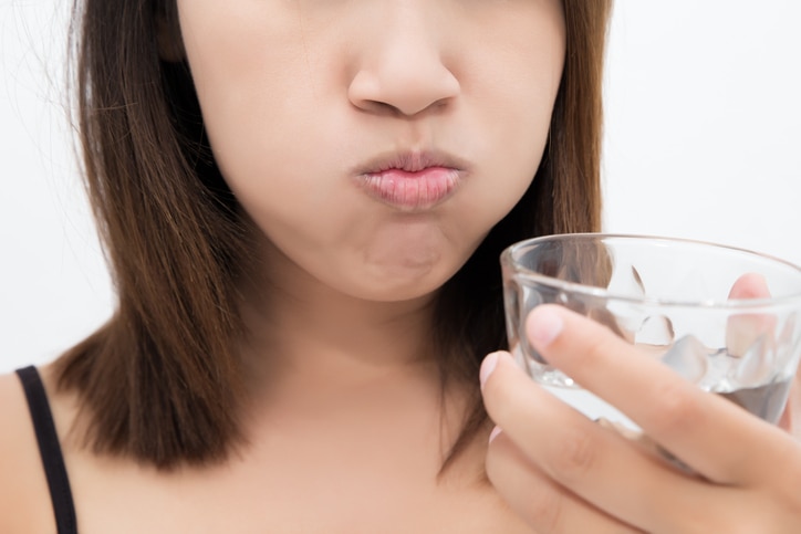 Healthy happy woman rinsing and gargling while using mouthwash from a glass, During daily oral hygiene routine, Portrait with bare shoulders, Dental Health Concepts