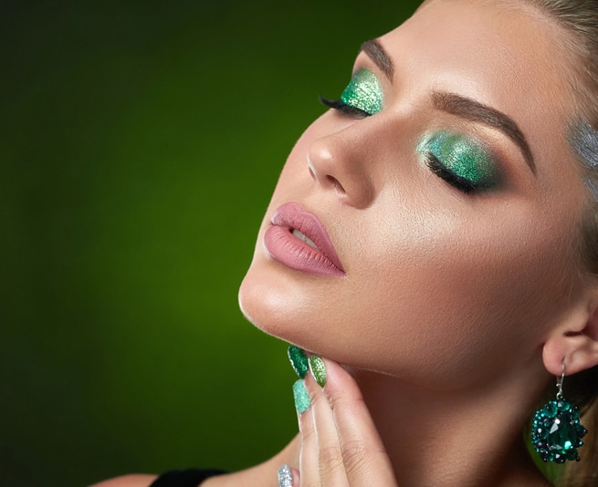 Seductive and sensual brunette girl with shiny manicure, makeup in green colors, touching neck and chin. Beautiful woman with closed eyes, big rounded earring posing at studio.