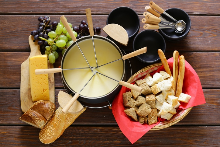 Traditional set of utensils for fondue, with bread, cheese, grapes