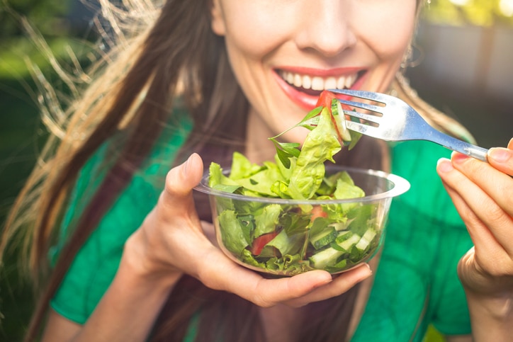 Woman eating healthy salad, focus on fork with salad