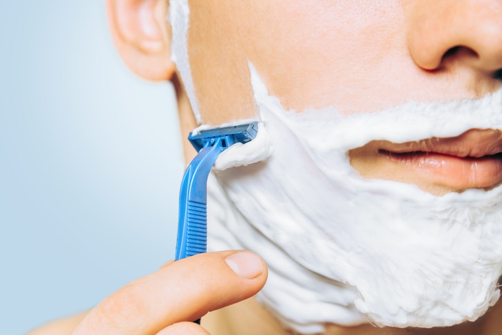 Man with foam on his face is shaving with razor, close-up