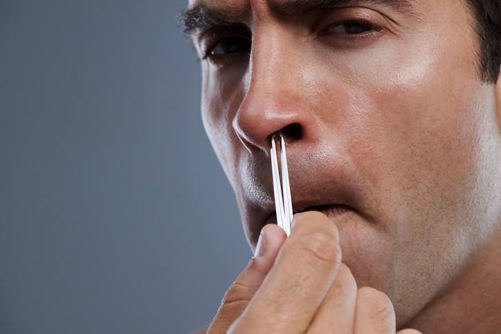 Closeup studio shot of a young man plucking his nosehair