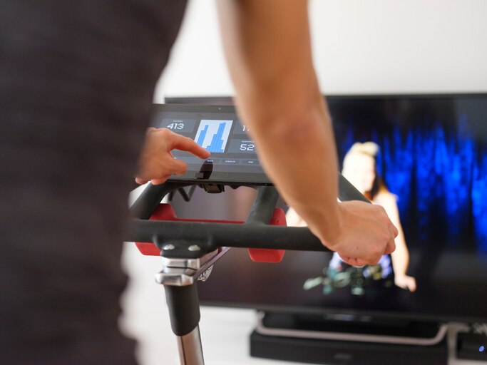 A woman exercising on a spin bike using an online instructor inside a home.