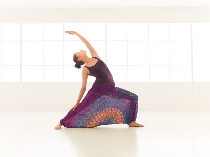 front view of young  woman in balanced yoga pose, dressed colorful indor studio