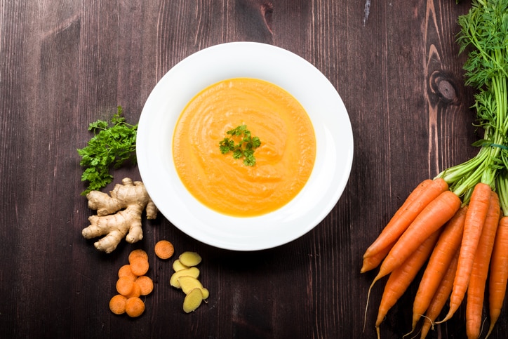 Fresh carrot ginger soup with ingredients on background