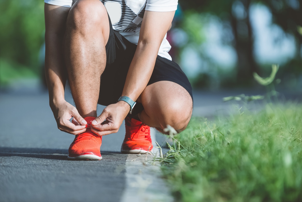 Running shoes runner man tying laces for autumn run in forest park. Runner trying running shoes getting ready for run. Jogging men exercise motivation heatlh and fitness.