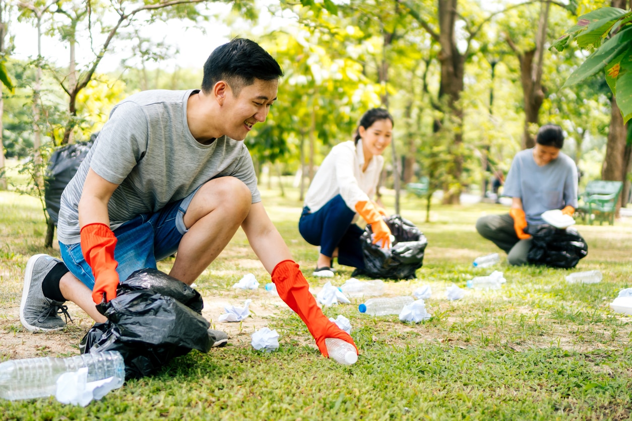 Young Asian man and women wearing orange gloves and collecting trash in garbage bag in the park. Save the earth and environmental concern concept